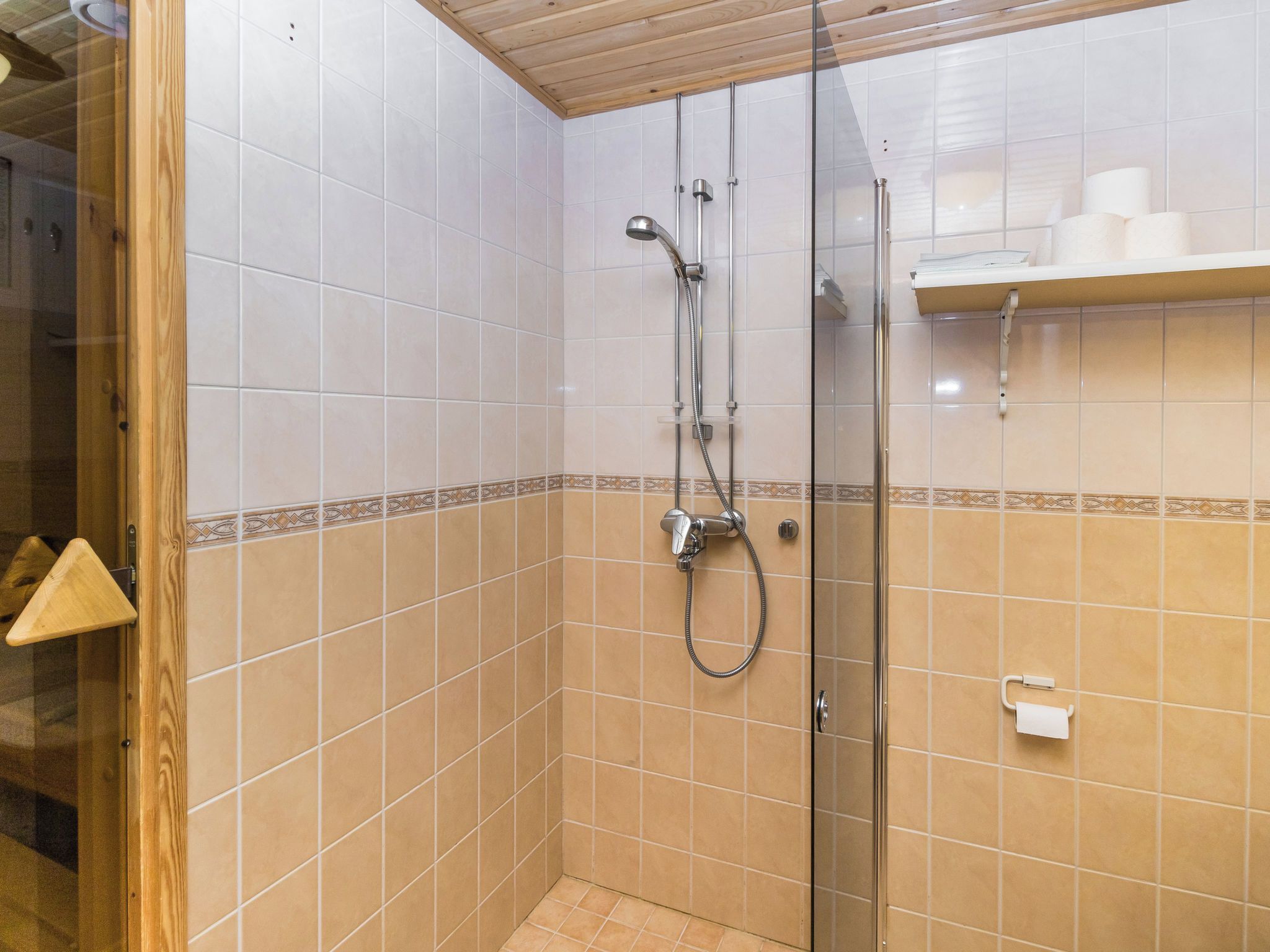 A shower area with a glass door, tiled walls, and a shelf with toiletries.