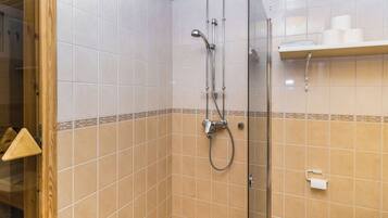 A shower area with a glass door, tiled walls, and a shelf with toiletries.