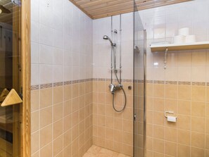 A shower area with a glass door, tiled walls, and a shelf with toiletries. - Rautulampi g14 by Interhome (Inari)