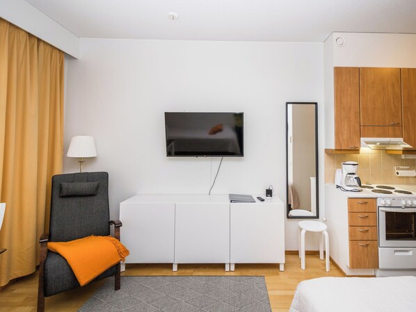A hotel room with a bed, a desk with a chair, a television, a mirror, a kitchenette, and a window with curtains. - Rautulampi g14 by Interhome (Inari)