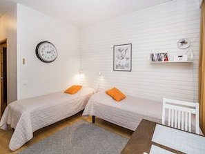 A small, clean room with two single beds, a wall clock, a framed picture, a bookshelf, and a white chair. - Rautulampi g14 by Interhome (Inari)