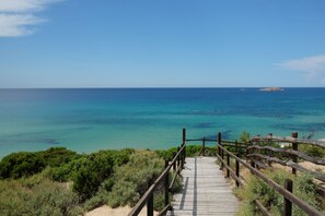 A wooden boardwalk leading to a beach with clear turquoise waters and a distant island.