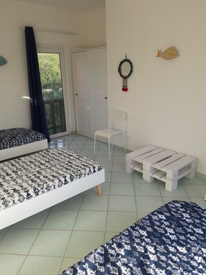 A bedroom with two beds, a white chair, a small white table, and a door leading to a balcony.