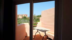 A balcony with a table and chairs, a view of greenery and buildings, and a clear sky.