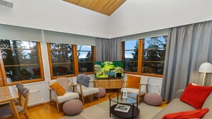Una sala de estar moderna con televisor, asientos y ventanas amplias.