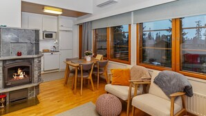 Una sala de estar moderna con chimenea, muebles de madera y ventanas grandes que dan a vista de árboles.