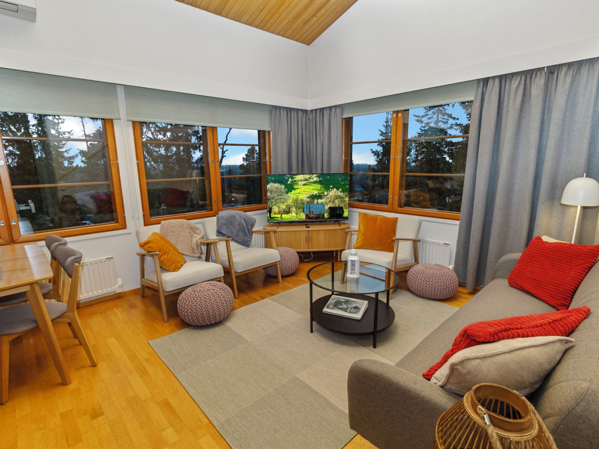 A modern living room with a television, seating, and large windows.