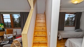 Una escalera de madera en una habitación moderna con una cama, un escritorio y un televisor.