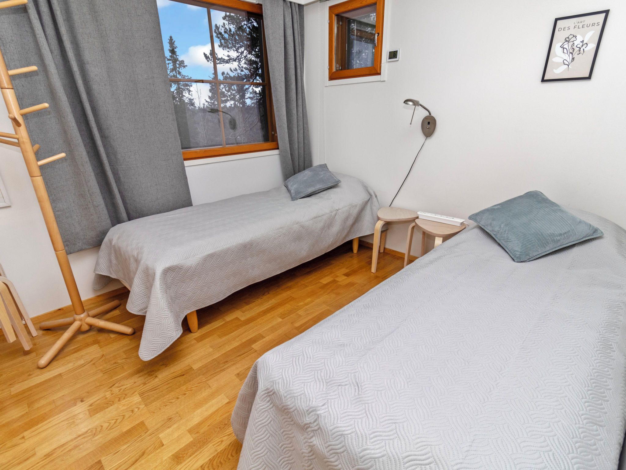 Une chambre avec deux lits simples, un plancher en bois, une fenêtre donnant sur les arbres, une table de chevet avec une lampe et une prise de courant murale.
