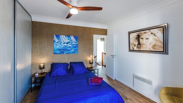 A bedroom with a large bed, a ceiling fan, a painting, a door, and a chair. - Villa Front de Mer - Presqu'île de Giens (Hyères)