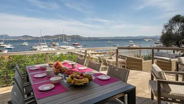 Ein Esstisch gedeckt mit Tellern, Schüsseln und Früchten, mit Blick auf eine Marina mit Booten und Hügeln in der Ferne.