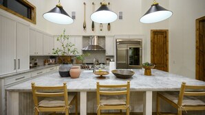 Cucina con mobili bianchi, un'isola grande con sedie, lampade a sospensione e un forno in acciaio inossidabile.