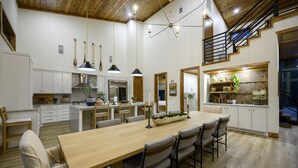 Un'ampia cucina con un tavolo da pranzo in legno, elettrodomestici moderni e una scala che conduce a un piano superiore.
