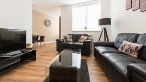 Ein modernes Wohnzimmer mit Flachbildfernseher, Ledersofas, einem Couchtisch und einem Essbereich mit Stühlen.