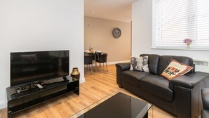 Ein modernes Wohnzimmer mit Flachbildfernseher, einer schwarzen Ledersofa und einem Essbereich mit Tisch und Stühlen.
