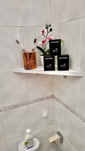 Un baño con pared de azulejos blancos, una repisa con orquídea en maceta y tres letreros de bienvenida negros.