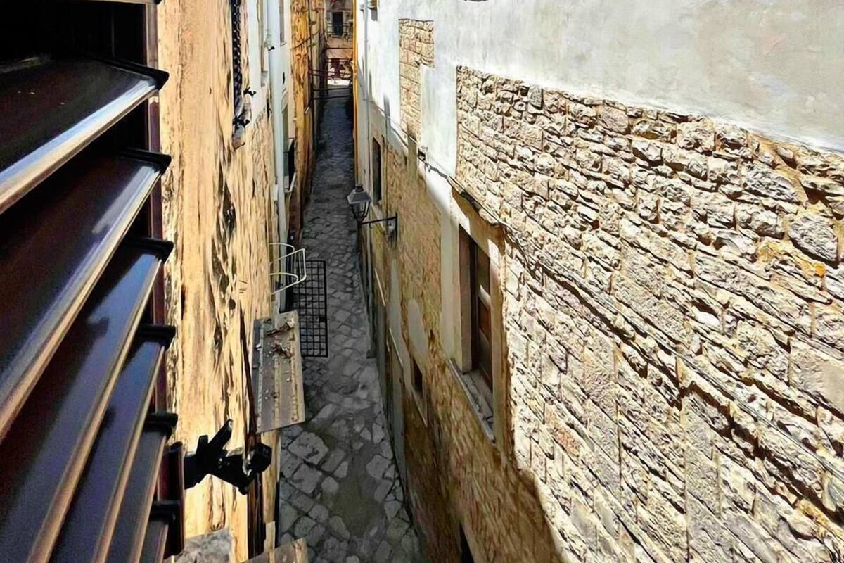 Une ruelle étroite pavée, bordée de bâtiments aux façades en pierre et aux volets métalliques.