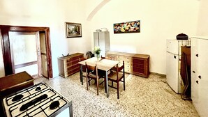 Eine Küche mit Gaskochfeld, Holzschränken, einem Esstisch mit Stühlen, einem Kühlschrank und zwei an der Wand hängenden Bildern.