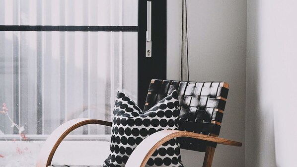A chair with a woven backrest and black and white patterned cushions, positioned near a window with vertical blinds.
