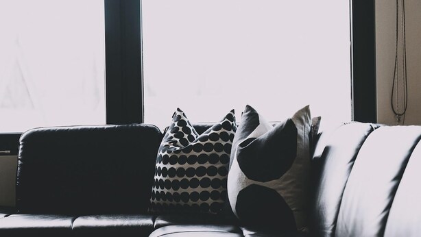 Um sofá de couro preto com almofadas estampadas em um quarto com grandes janelas.