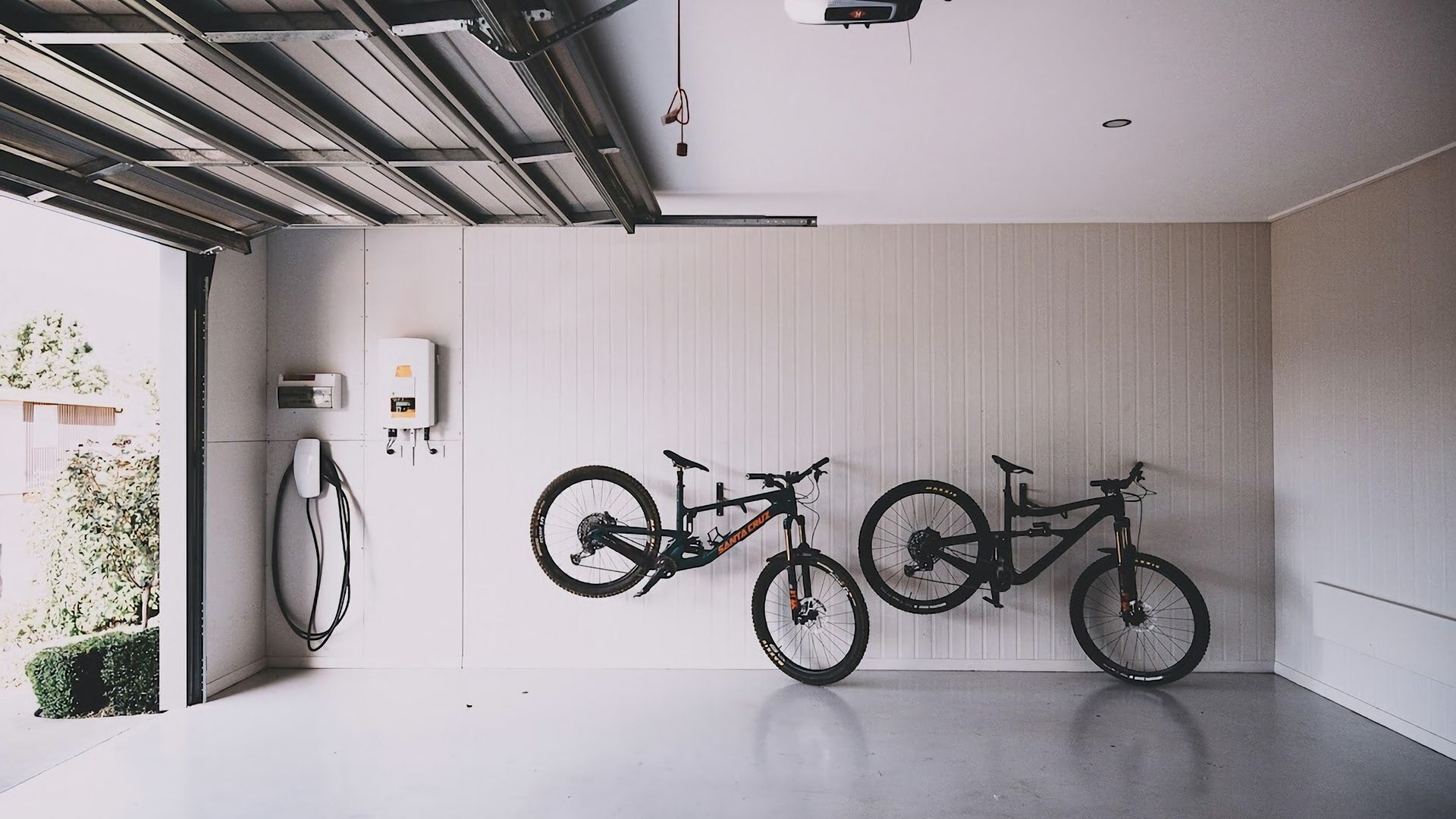 Un garaje con dos bicicletas colgadas en la pared, un calentador de agua y un enchufe.