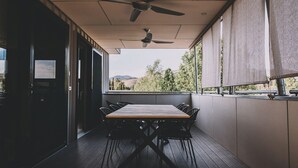 Uma área de refeições ao ar livre coberta, com mesa, cadeiras, ventilador de teto e vista para o exterior.