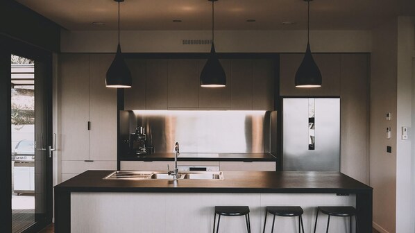 Une cuisine moderne dotée d’un îlot central, de luminaires suspendus et offrant une vue sur l’extérieur.