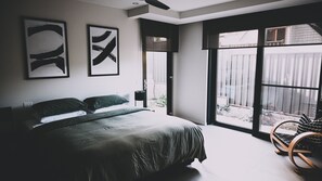 Une chambre avec un grand lit, deux œuvres d’art accrochées au mur, une fenêtre donnant sur un beau paysage et une chaise en bois.