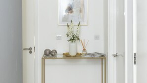 A hallway with a white door, a framed abstract painting, a small table with decorative items, and a light-colored wooden floor. - Stylish 2BR Apartment, Town Centre, Free Parking (Hatfield)