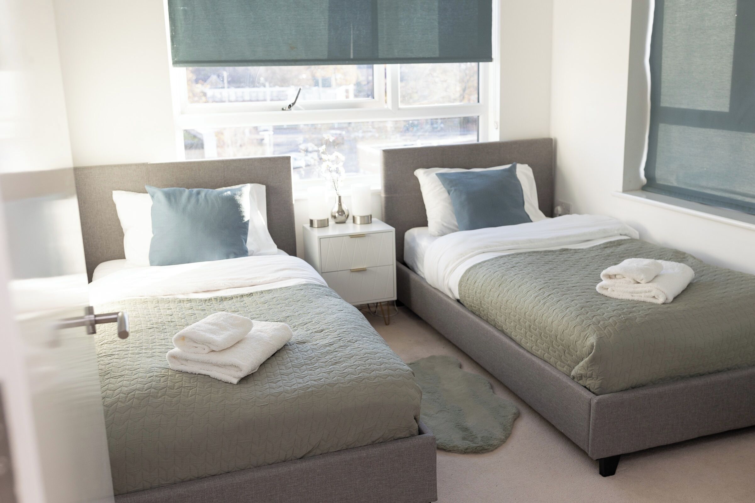 A hotel room with two beds, each with a pillow and a folded towel. There is a window with a view of buildings outside.