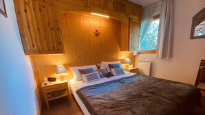 A cozy room with a wooden ceiling, a bed with a dark blanket, two bedside tables with lamps, and a window with curtains. - Cozy apartment for 6, near slopes, includes parking (Peisey-Nancroix-Plan Peisey)