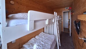 A wooden cabin room with bunk beds, a door, and a wall-mounted heater.