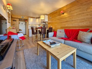 A cozy living area with a sofa, coffee table, and chairs, a kitchen with wooden walls, and a dining table.