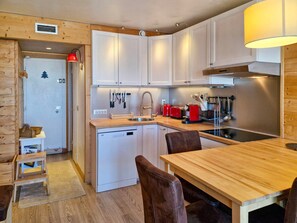 A compact kitchen with white cabinets, a wooden countertop, a sink, a red toaster, and a dining area with a wooden table and chairs.
