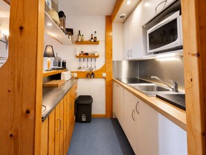 Eine kleine Küche mit Holzausstattung, einem Edelstahlspülbecken und einer Mikrowelle.