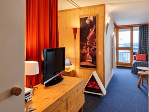 A hotel room with a wooden cabinet, a television, a fireplace, a poster, and a view of the outdoors.
