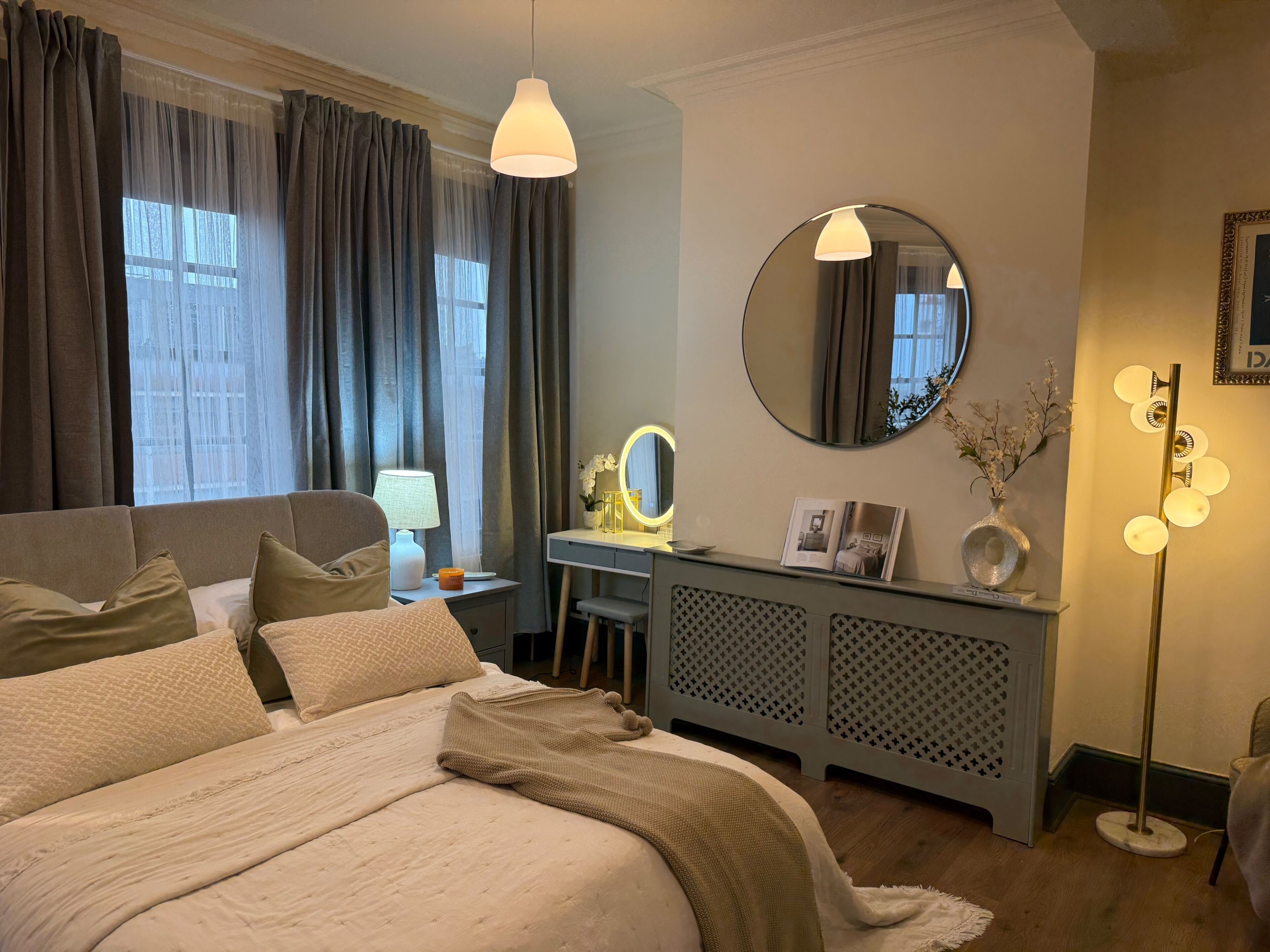 A hotel room with a bed, a vanity with a mirror, a desk, and a standing lamp.