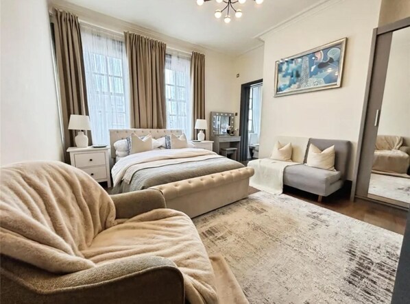 Une chambre avec un grand lit, un canapé, un bureau avec un miroir et un tableau au mur.
