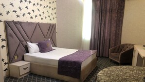 Una habitación de hotel con una cama, una silla, una mesita y una alfombra estampada.