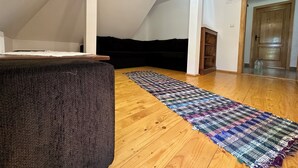 A room with a sloped ceiling, a black sofa, a colorful woven rug, and a wooden floor. - Cazare Apuseni  Pensiune cu ciubăr (Vidra)