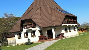 A traditional chalet with a steeply pitched roof, a balcony with flower boxes, and a gravel pathway leading to the entrance. - Cazare Apuseni  Pensiune cu ciubăr (Vidra)