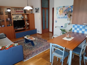 Un salon comprenant un canapé, un téléviseur, un meuble en bois et un coin repas avec une table et des chaises.