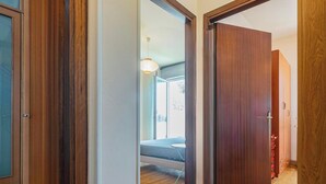 A hallway with wooden doors and a view into a room with a bed and a hanging light fixture.