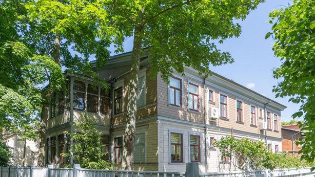 Een gebouw met twee verdiepingen, een witte hekken, grote ramen en een overdekte veranda.