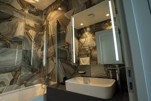 Une salle de bain moderne avec un mur en marbre, un lavabo rectangulaire et une douche à parois de verre.