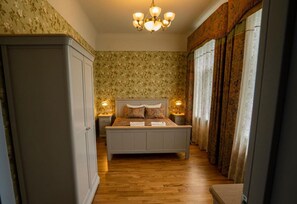 Un couloir étroit mène à une chambre à coucher qui contient un lit, deux tables de chevet avec des lampes et une armoire.