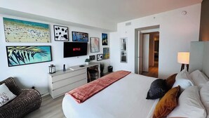 A hotel room with a large bed, a desk with a computer, a TV displaying Netflix, and various framed artworks on the walls. - Ocean-View Corner 1BR-1BA - 18th Floor, LYFE Resort & Residences (Hollywood)