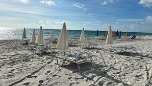 A beach with white and blue umbrellas, sun loungers, and a clear sky. - Ocean-View Corner 1BR-1BA - 18th Floor, LYFE Resort & Residences (Hollywood)
