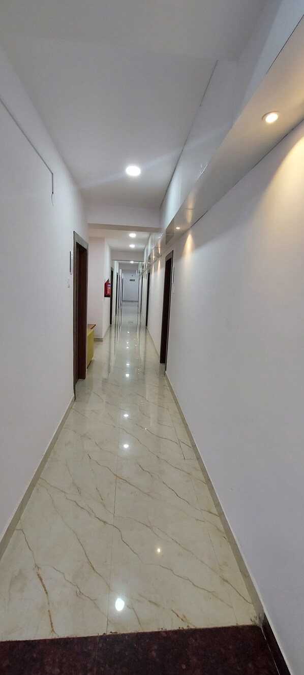 A long, narrow hallway with white walls and a marble floor.