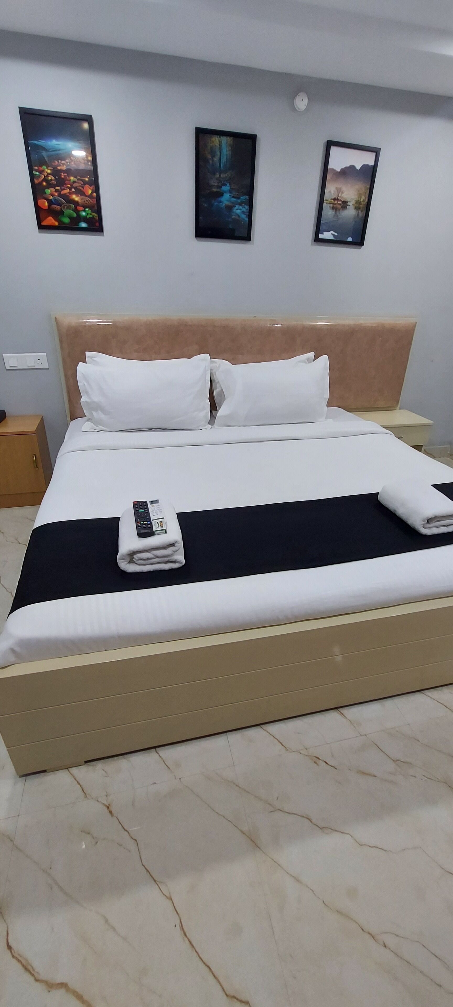 Een netjes opgemaakt bed met witte lakens en een zwart dekbed, een afstandsbediening en een opgevouwen handdoek op het bed.